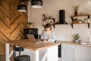 Small business owner learning and planning with a laptop and notebook at a kitchen workspace, researching AI tools to improve productivity and business decision-making