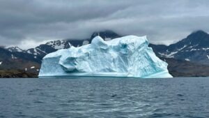 A massive white and blue iceberg rises from a dark arctic sea, with snow-capped rocky mountains in the background under an overcast sky, illustrating the hidden scale of AI workforce exposure measured by the MIT Iceberg Index
