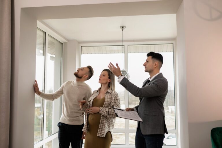 Real estate agent showing a bright, modern home interior to a couple during a property tour on a sunny afternoon