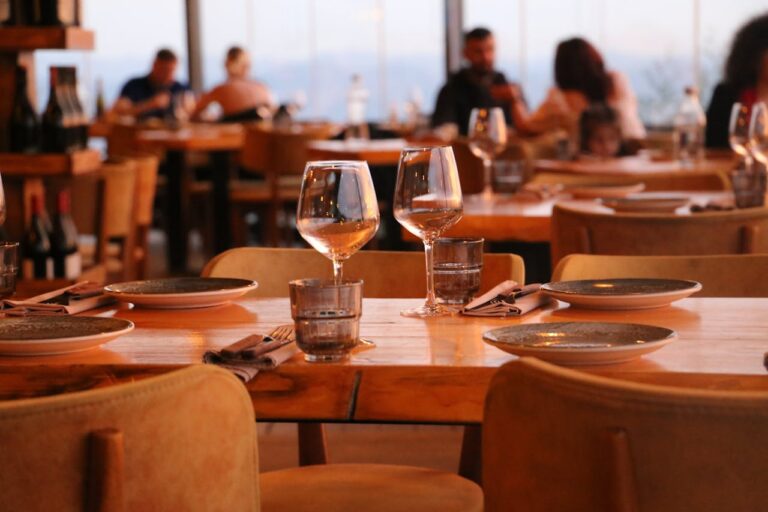 Warmly lit restaurant dining room set for evening service with white tablecloths, candles, and neatly arranged place settings