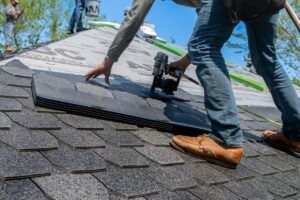 Roofing contractor installing asphalt shingles on a residential roof with a pneumatic nail gun on a sunny day