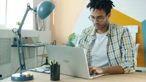 A small business owner working on a laptop, researching AI automation tools like Zapier, Make.com, and N8N to streamline his workflow.
