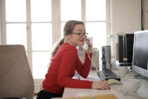 Small business owner in a red sweater answering a landline phone call at her office desk